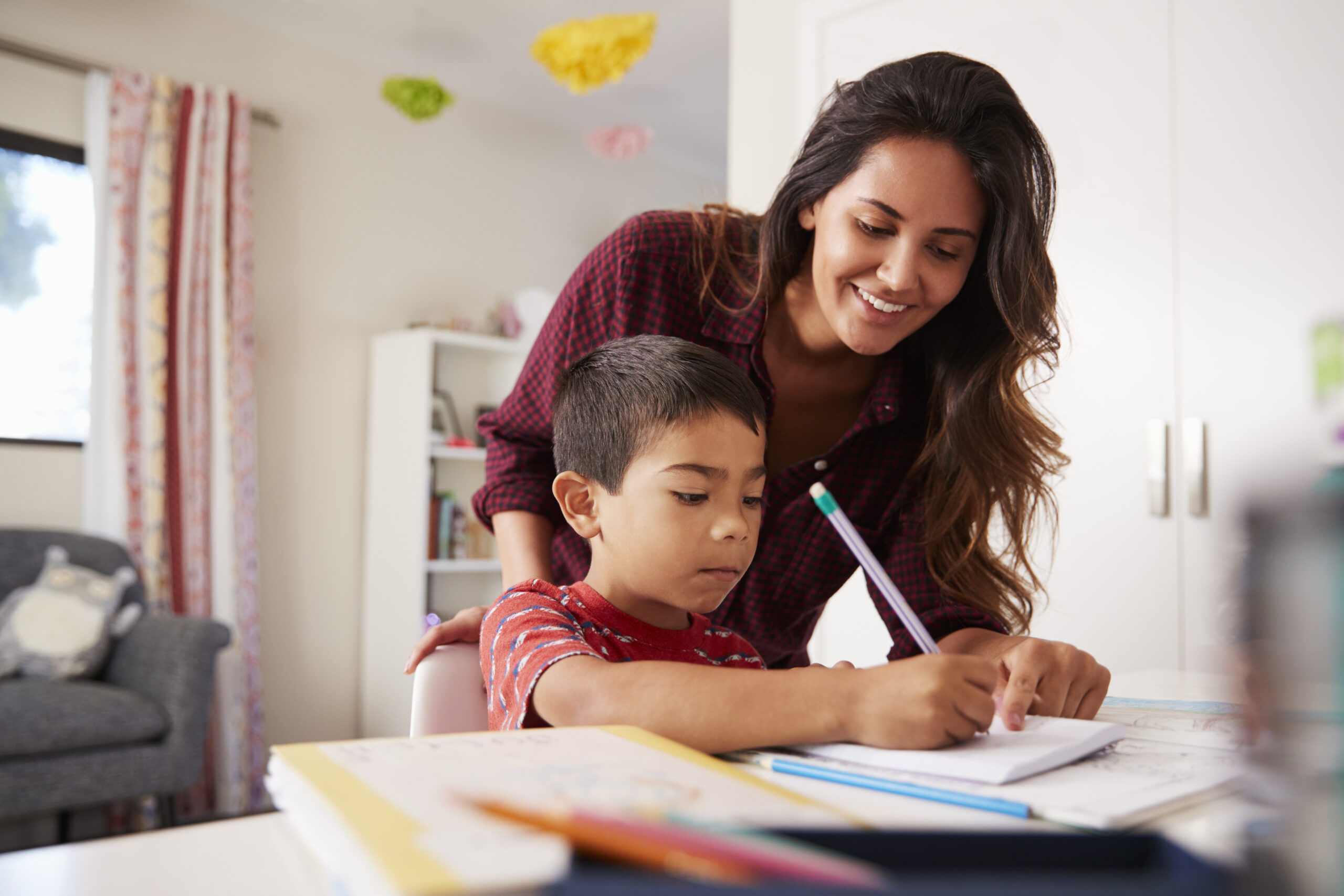 Mother Helping Son With Homework Sitting At Desk In Bedroom Father and siblings drawing pictures with pencils